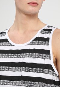 Schwarz-weiß gestreifes Tanktop mit einer aufgesetzten Tasche. Die Streifen zeigen unterschiedliche Texturen und Muster und bestehen aus leichtem Stoff.