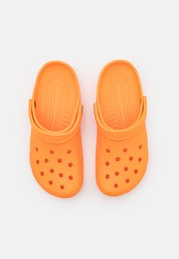Zuecos de espuma naranja con una plantilla texturizada y múltiples agujeros de ventilación, que cuentan con una correa ajustable en el talón para un ajuste seguro.
