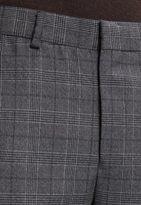 Szare spodnie w kratę z fakturowanej tkaniny. Posiadają płaski przód, paski na pasek oraz subtelne wzory w kratę w czerni i bieli.