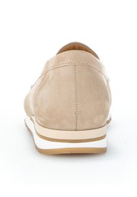 Beige suède sneakers met een afgeronde vorm, witte tussenzool en bruine accenten. Minimalistisch ontwerp met zichtbare stiksel op de achterkant.