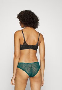 Czarny koronkowy stanik z regulowanymi ramiączkami i zapięciem na haftkę, w zestawie z turkusowymi koronkowymi majtkami z falbaniastym brzegiem i wzorem.