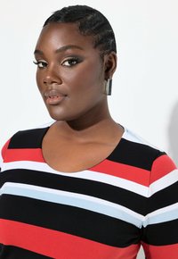 Raidallinen t-paita mustana, punaisena, vaaleansinisenä ja valkoisena, jossa on pyöreä kaula-aukko. Mallilla on metallic neliökorvakorut; sileä kankaan tekstuuri.