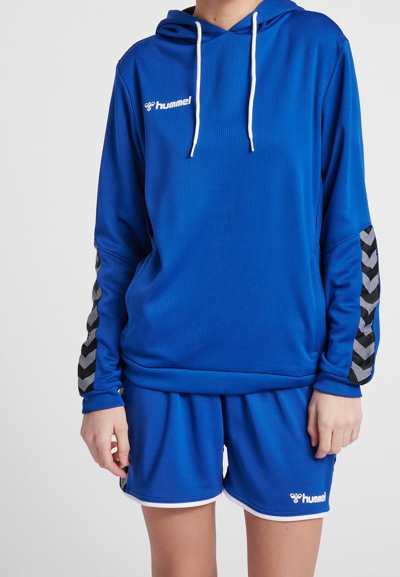 Set di felpa blu con cappuccio e pantaloni corti realizzati in tessuto testurizzato. La felpa presenta una tasca frontale, cordini e accenti a zigzag neri e grigi sulle maniche.
