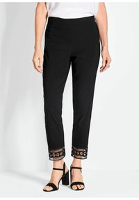 Zwarte broek met een elastische tailleband, tapered fit en decoratieve geborduurde zoom met geometrische patronen. Gecombineerd met zwarte hoge hakken sandalen.