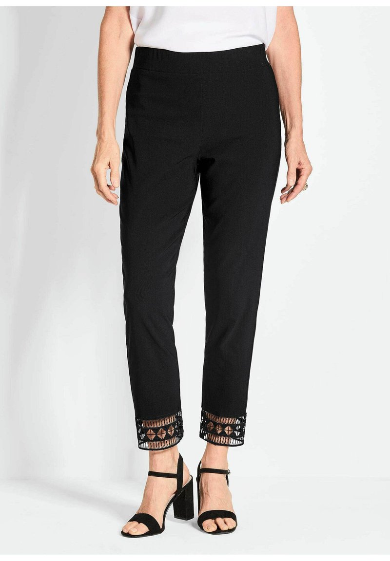 Zwarte broek met een elastische tailleband, tapered fit en decoratieve geborduurde zoom met geometrische patronen. Gecombineerd met zwarte hoge hakken sandalen.