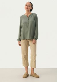 Olivengrøn langærmet bluse med henley-udskæring og knapdetaljer, parret med beige cropped bukser og tan slip-on sko.