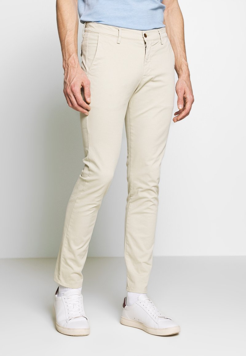 Lichtbeige katoenen chinos hebben een slim fit met riemlussen, een ritssluiting en voorzakken. Draag ze met witte sneakers en een blauwe blouse.