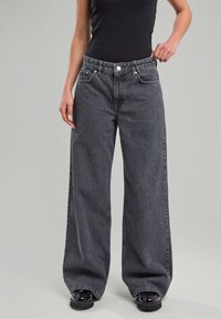 Wide-leg jeans in black with vertical ribbed texture, featuring front pockets, a button closure, and a relaxed fit. Smooth fabric finish.