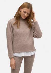 Suéter marrón con canalé, cuello alto y hombros caídos, combinado con una camisa blanca. Textura suave y corte ligeramente holgado.