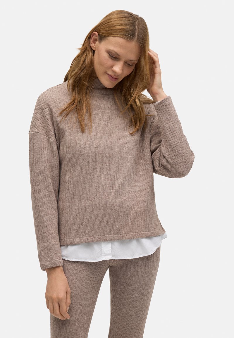 Suéter marrón con canalé, cuello alto y hombros caídos, combinado con una camisa blanca. Textura suave y corte ligeramente holgado.