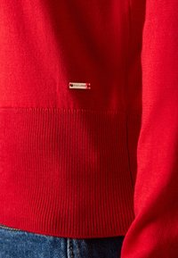 Red knit sweater with ribbed hem and cuffs. Includes a small branded tag labeled "Holly & Whyte." Smooth texture, fitted design.