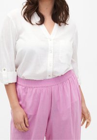 Blusa di lino bianca con scollo a V e dettagli con bottoni, abbinata a pantaloni rosa leggeri con vita elastica. Tessuti testurizzati, vestibilità comoda.