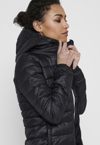 Black puffer jacket with a zippered front, high collar, and hood. Features quilted texture and elastic cuffs for a snug fit.