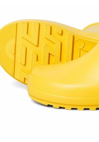 Bottes en caoutchouc jaunes avec une surface supérieure lisse et une semelle texturée présentant un motif de crampons pour une meilleure adhérence et traction.