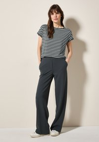 Camisa de manga corta a rayas en verde oscuro y blanco, combinada con pantalones oscuros de pierna ancha y talle alto en gris oscuro. La modelo lleva zapatillas blancas.
