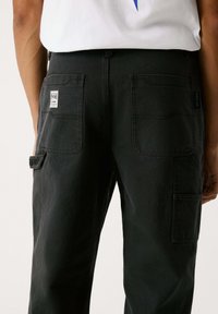 Schwarze Cargo-Hosen aus Baumwolle mit großen Seiten- und Gesäßtaschen sowie einem kleinen Logo-Tag auf der rechten Tasche, im geraden Schnitt.