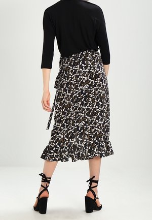 Femme portant une jupe midi noire à motifs floraux avec un ourlet à volants, un haut noir à manches trois-quarts et des chaussures à talons hauts noires à lacets, vue de dos.