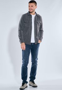 Gray corduroy shirt jacket with two chest pockets, worn over a white t-shirt, paired with dark jeans and gray sneakers.