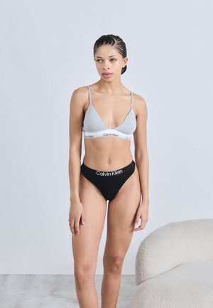 Γκρι βαμβακερό σουτιέν με λεπτές τιράντες και χαμηλό ντεκολτέ, σε συνδυασμό με μαύρο βαμβακερό στρινγκ με το λογότυπο "Calvin Klein" σε λευκό.