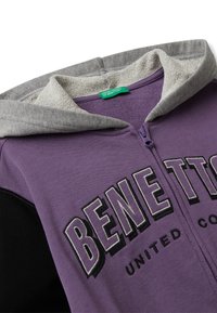 Paarse rits-hoodie met grijze binnenvoering in de capuchon, zwarte mouwen en de tekst "BENETTON" geborduurd op de borst.