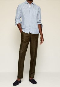 Light blue and white striped button-up shirt with a chest pocket, paired with olive green pants and navy slip-on shoes.