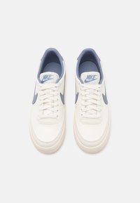 Vita lädersneakers med låg design, blå detaljer på Swoosh och tunga, samt texturerade snören, med en ljusfärgad sula.