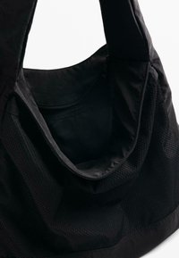 Zwarte stoffen draagtas met een gladde textuur en mesh details. Afgeronde bovenopening en stevige hengsels om te dragen. Het interieur heeft een ritszak.