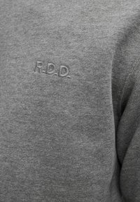 Felpa grigia realizzata in tessuto morbido, con un piccolo logo "R.D.D." in rilievo sul petto, caratterizzata da una superficie liscia e senza fantasia.