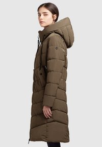 Dugo maslinasto zeleni puffer kaput s kapuljačom, s ušivenim uzorkom, zatvaranjem na vezicu i bočnim džepovima. Glatka, teksturirana tkanina.