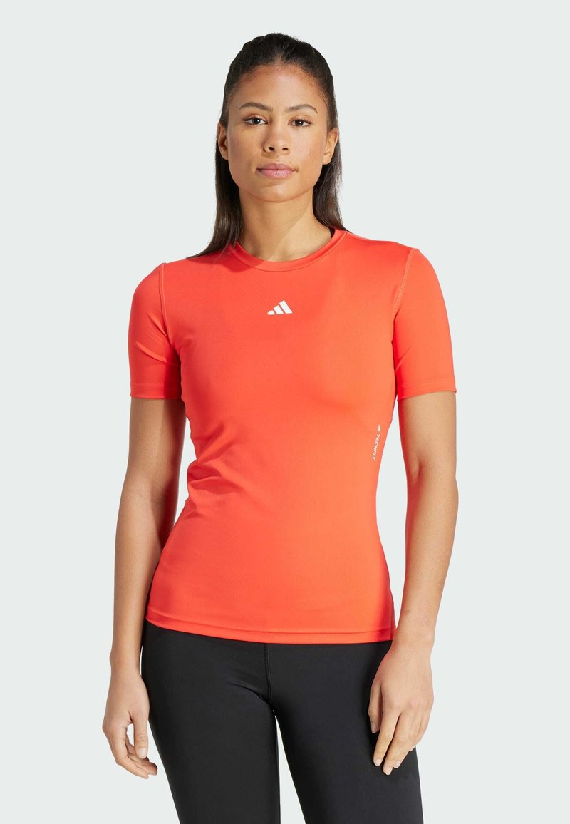 Camiseta atlética de manga corta, ajustada al cuerpo, en un vibrante color naranja con un cuello redondo y un logo blanco cerca del pecho, fabricada en un tejido suave.