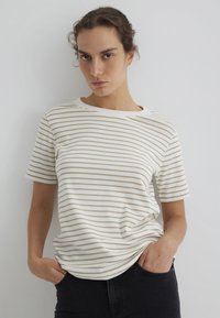 Kurzärmeliges T-Shirt aus weicher Baumwolle, mit horizontalen beigen Streifen auf weißem Hintergrund, locker sitzend und mit rundem Ausschnitt.