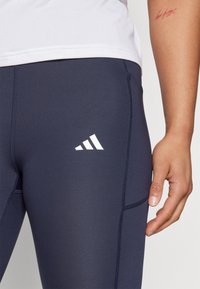 Leggings sportivi blu navy con una texture liscia, dotati di logo bianco e cuciture in contrasto per un tocco di dettaglio.