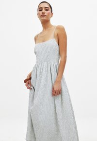 Robe sans manches à rayures avec un corsage ajusté et une jupe fluide, en tissu léger de couleur blanche avec des rayures bleues.