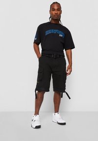 Sort T-shirt med blåt "REDEFINED" print, parret med sorte cargo shorts med sidelommer og et bælte. Hvide sneakers fuldender outfittet.