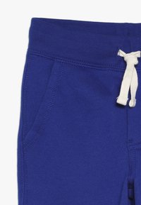 Pantalones de chándal azules hechos de una tela suave. Cintura elástica con cordón blanco, bolsillos laterales y detalles de costura visibles.