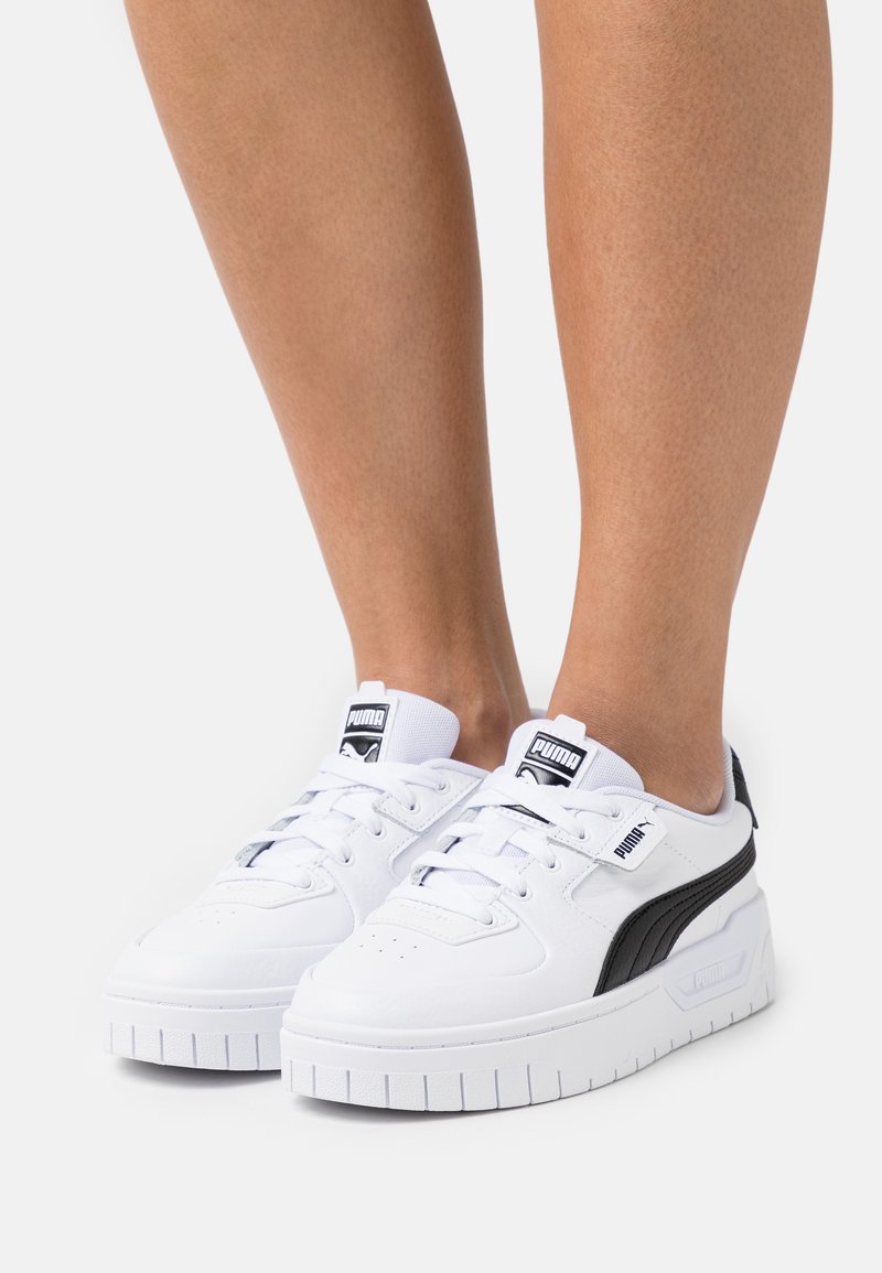 Baskets blanches avec un dessus en cuir texturé, accents noirs, semelle blanche épaisse et un logo sur la languette. Design lacé avec un col rembourré.