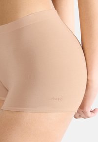 Beige nahtlose Boyshorts mit einer glatten Textur, ausgestattet mit einem breiten Bund und einem dezenten Logo-Detail am Saum.