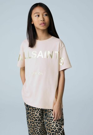 Hellrosa T-Shirt mit kurzen Ärmeln, goldfarbenem „ALLSAINTS“-Schriftzug und darunter „LONDON“, kombiniert mit schwarzen und braunen Leopardenmuster-Hosen.