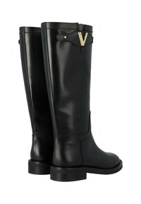 Bottes noires en cuir, montantes jusqu'au genou, avec une finition lisse, présentant un accent doré en forme de "V" en haut et un talon plat. Détail de piqûre sur la couture latérale visible.