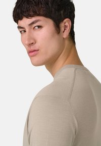 Camicia beige aderente con scollo rotondo e maniche corte, caratterizzata da una texture liscia e dettagli sottili delle cuciture.