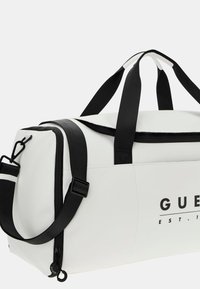 White duffel bag made of smooth, durable material featuring black straps, logo print, and a zippered closure with adjustable strap hardware.