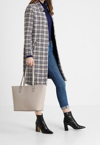 Skjorteblazer med lange ærmer, blå top, blå jeans, sorte ankelstøvler og en beige tote taske med dobbelthåndtag. Tekstureret stof og struktureret design.