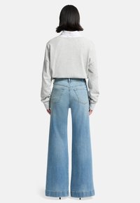 Gray oversized sweater and high-waisted light blue wide-leg denim jeans. Jeans feature a frayed hem and five pockets.
