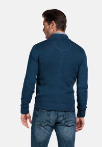 Navyblauwe gebreide trui met een hoge kraag, geribde manchetten en zoom. De stof lijkt zacht met een subtiele textuur. G gedragen met denim jeans.
