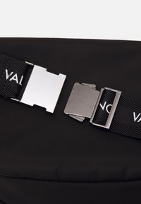 Svart tygrem med vit text och en öppen silverfärgad metallspänne på en svart bakgrund.