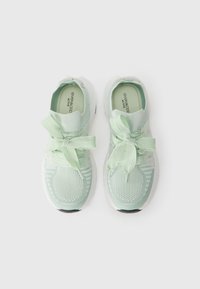 Light green athletic shoes featuring a mesh upper, ribbon laces, textured accents, and a white outsole with a black accent at the heel.