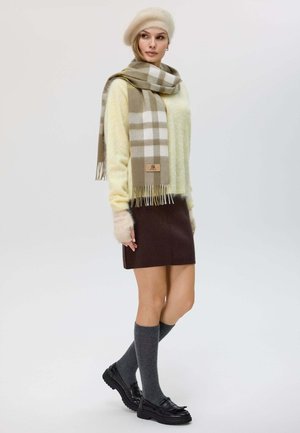 Sciarpa a quadri beige, maglione fuzzy giallo chiaro, gonna marrone, calze grigie al ginocchio e scarpe nere. Tessuti morbidi e design a strati.