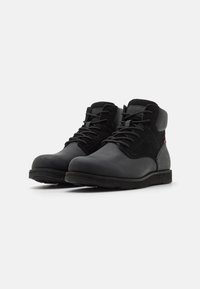 Botas negras hasta el tobillo que combinan cuero liso y ante. Punta redonda, diseño con cordones, suela plana de goma y sutil detalle en rojo.