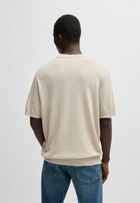 Light beige knitted short-sleeve sweater with round neckline, ribbed hem, and soft texture, worn with blue jeans. Rückenansicht.