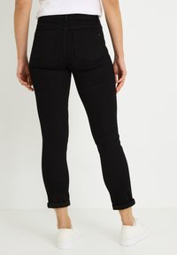 Jeans negros ajustados de talle medio, con cinco bolsillos y puños enrollados, hechos de denim elástico. Combinados con zapatos blancos sin cordones.